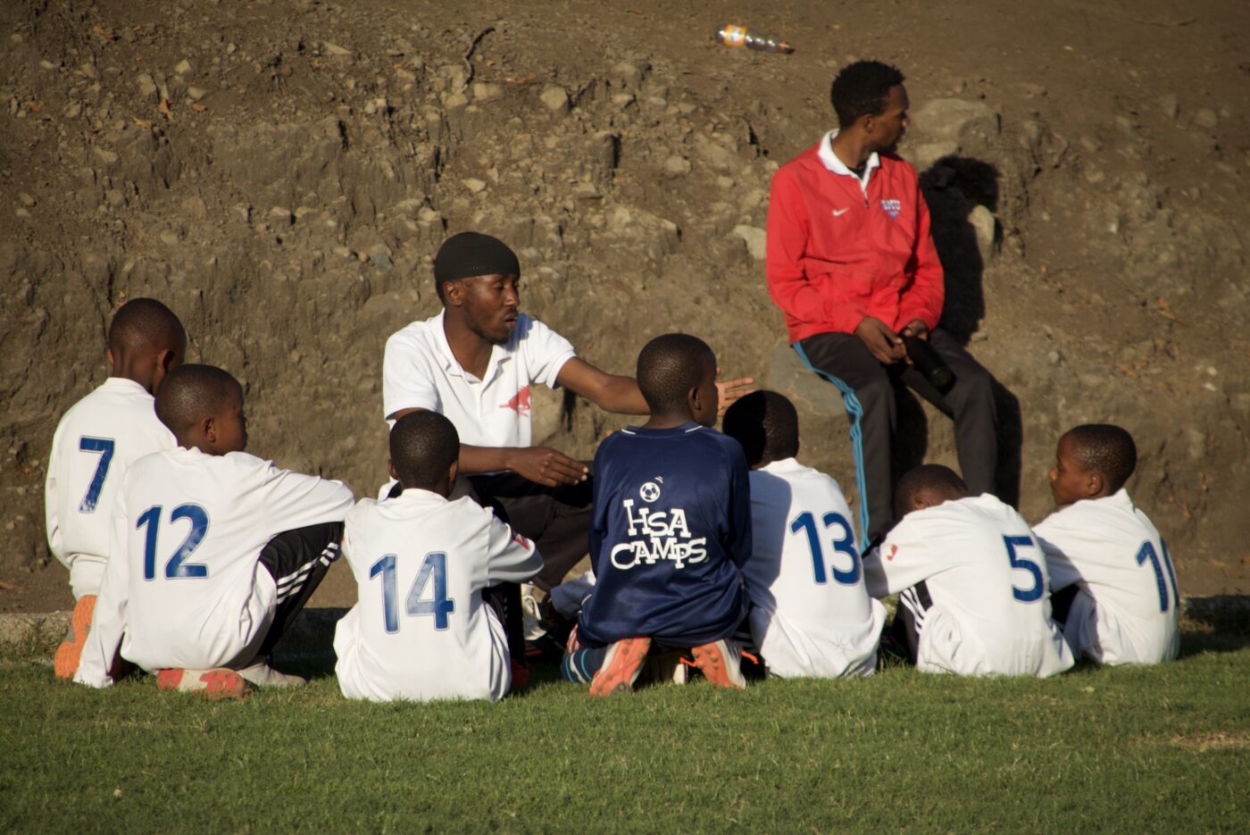 A coach talking with the squad on the touchline before a league match