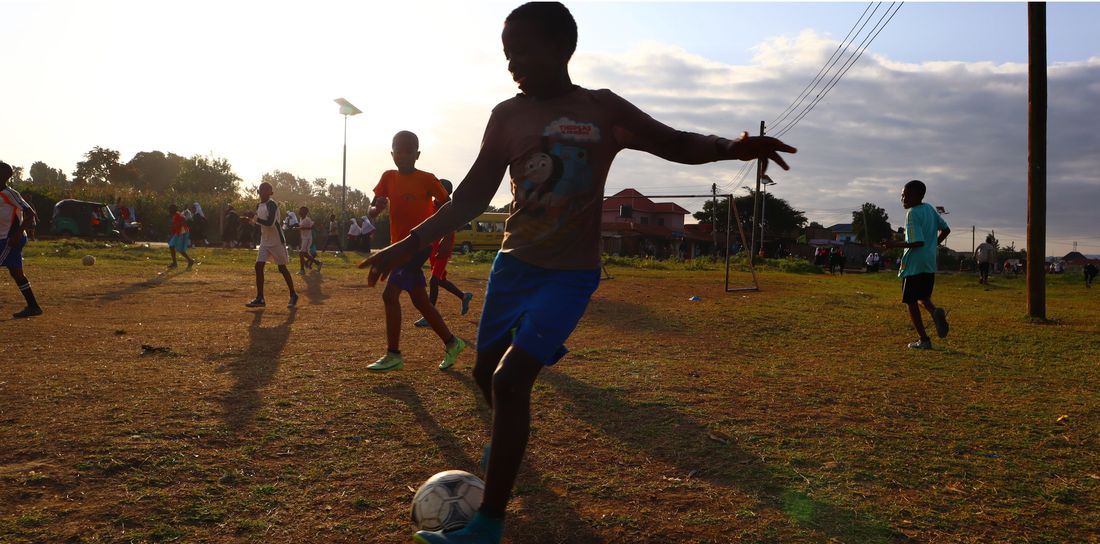 Satino players training on rough ground at sunset, one about to strike a football