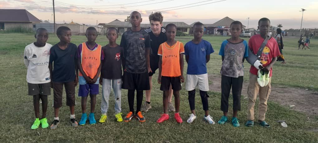 Nine Satino players lined up in newly donated football boots alongside Flip, a volunteer from the Netherlands